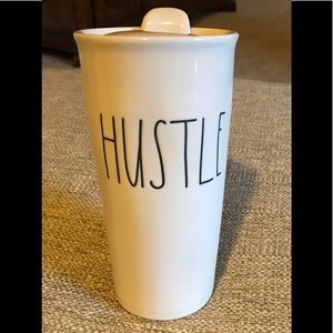 Rae Dunn tall mug with lid. It has Hustle on front